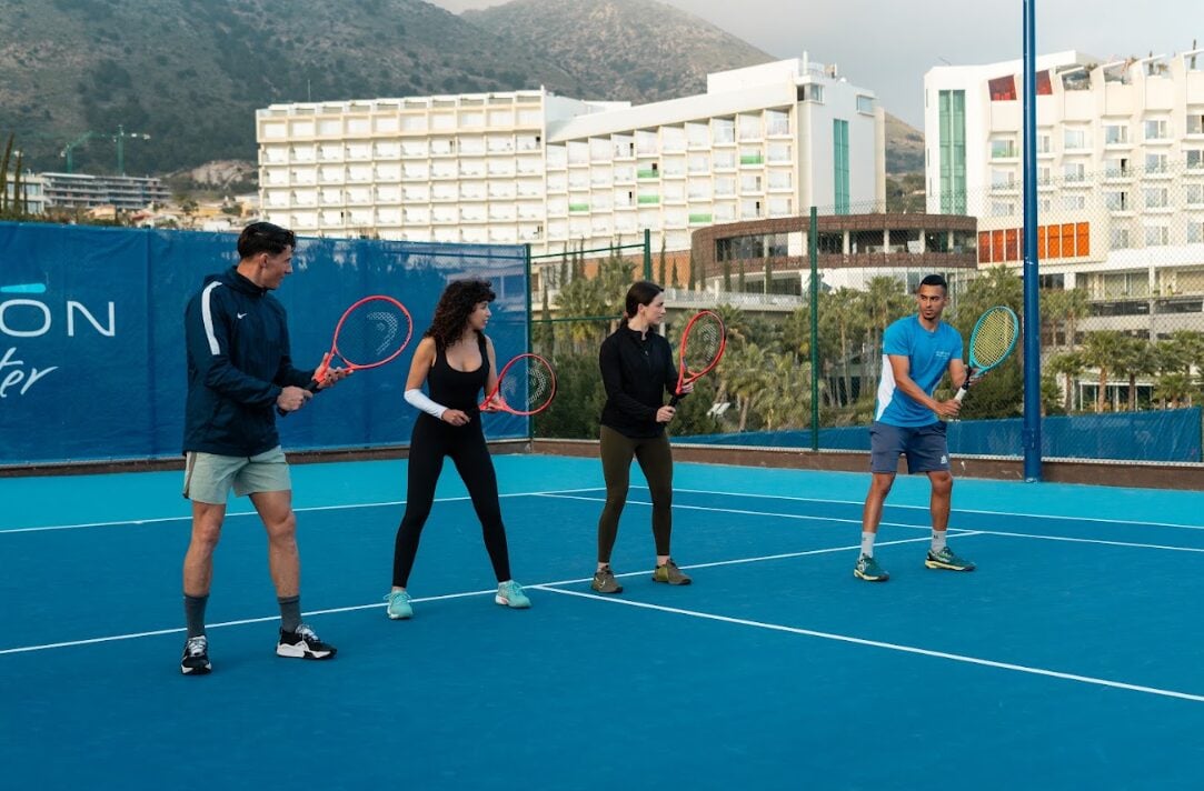 Grupo de jugadores en una clase de tenis en pista dura del Higuerón Tennis Center, con el resort al fondo en la Costa del Sol