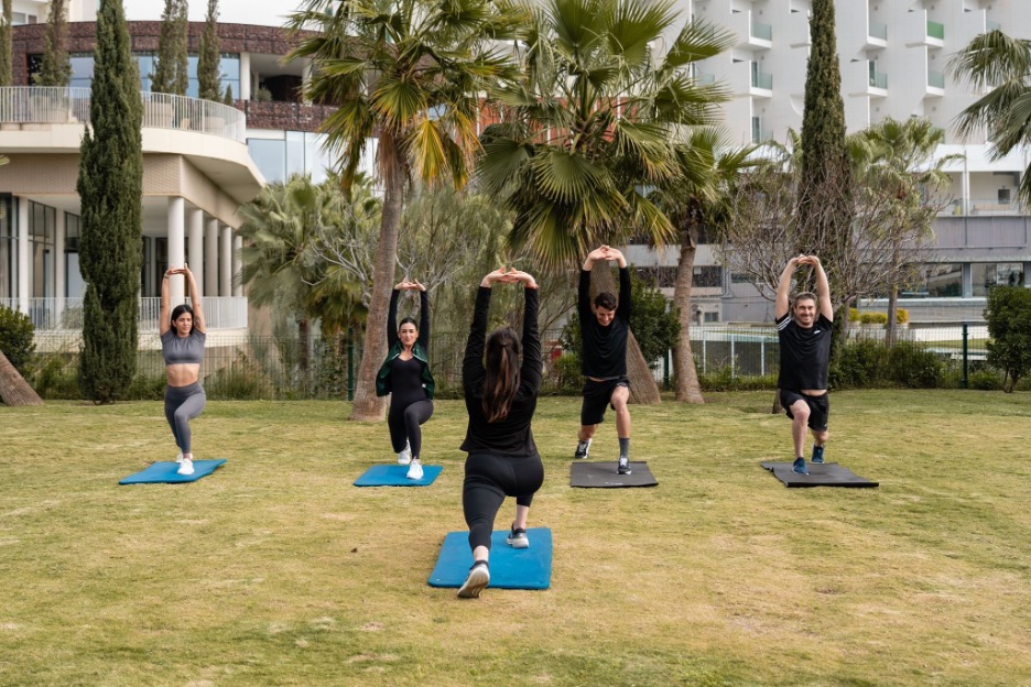 Clase de yoga al aire libre en el jardín de Higuerón Resort, con esterillas sobre césped y edificios del resort al fondo